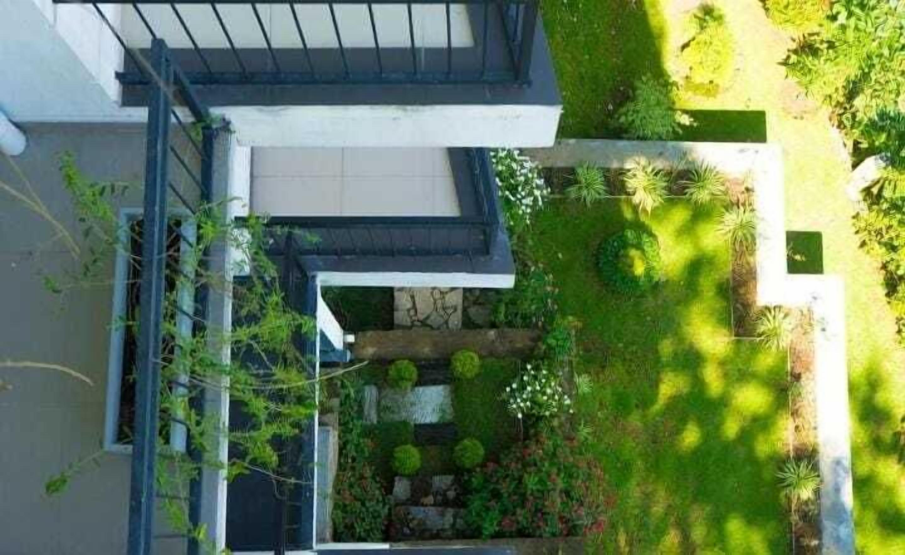 A modern house with a flat roof, a visible staircase, and a well-maintained garden with various plants and a small pond.