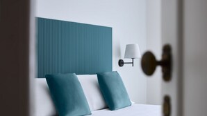 A modern hotel room with a bed, teal pillows, a white headboard, and a wall-mounted lamp. - Domus Modista (Vatican Museums / Sistine Chapel) (Roma)