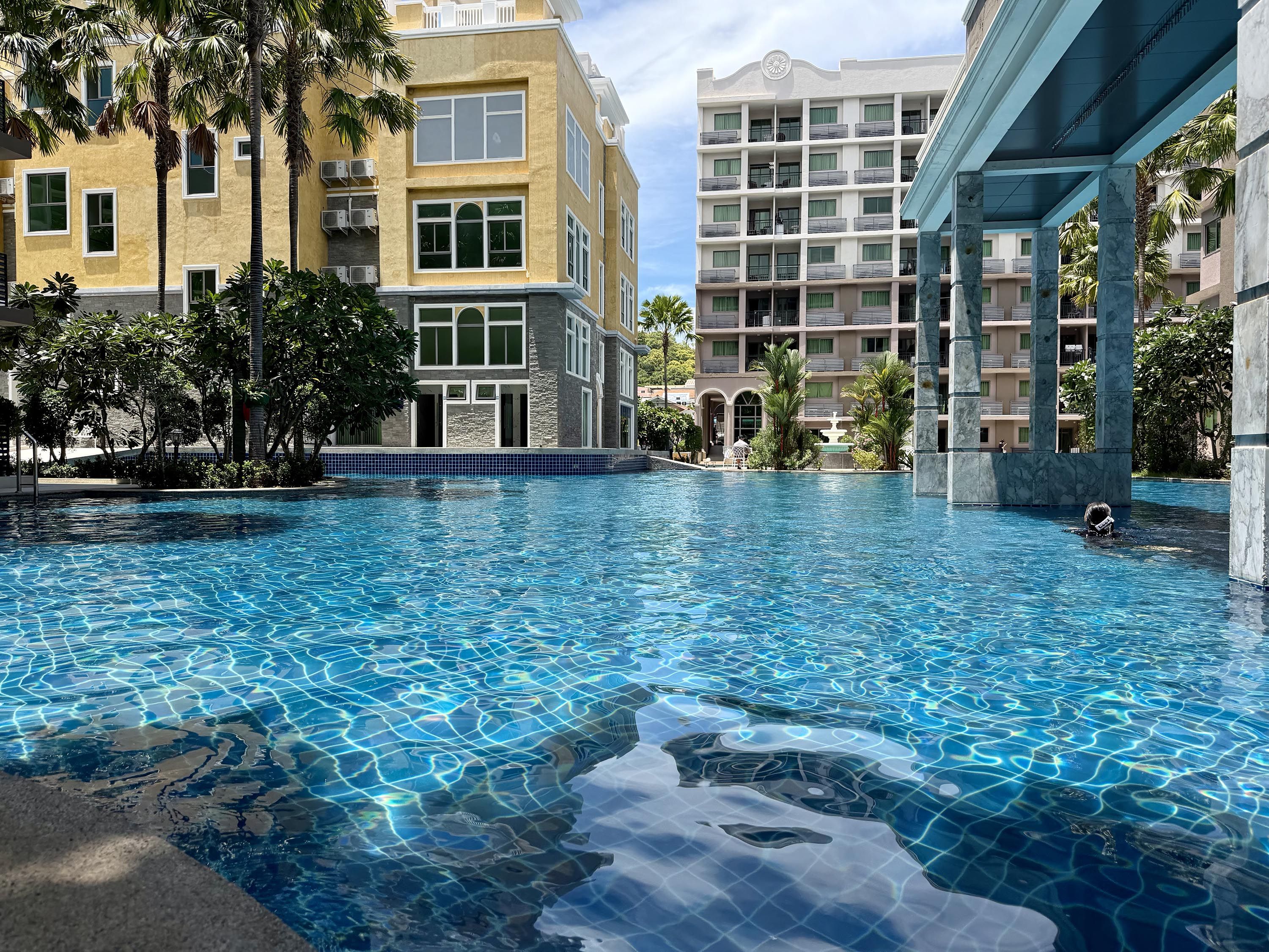 A swimming pool with clear blue water, surrounded by buildings with balconies and air conditioning units.