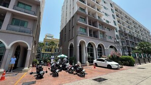A multi-story building with balconies, a parking area with motorcycles, and a white car parked on the street. - Arcadia Beach Continental (Pattaya)
