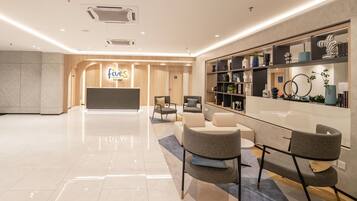 A modern hotel lobby with a reception desk, seating area, and a bookshelf.