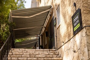 A stone building with a staircase, a striped awning, and a sign in Hebrew. - Artistic Vibes Haifa Hub by Sea N' Rent (Haifa)