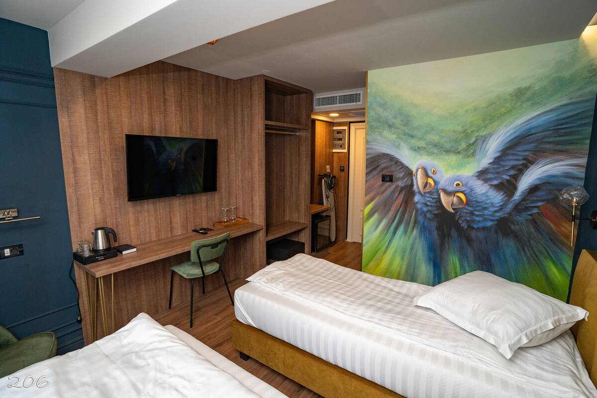 Ein Hotelzimmer mit Bett, Schreibtisch, Fernseher und einem Vogelgemälde.