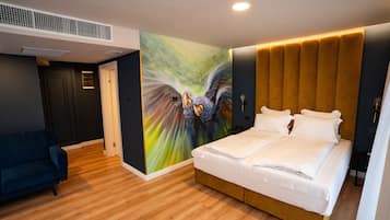 A hotel room with a large bed, a blue armchair, a colorful mural, and a modern headboard.