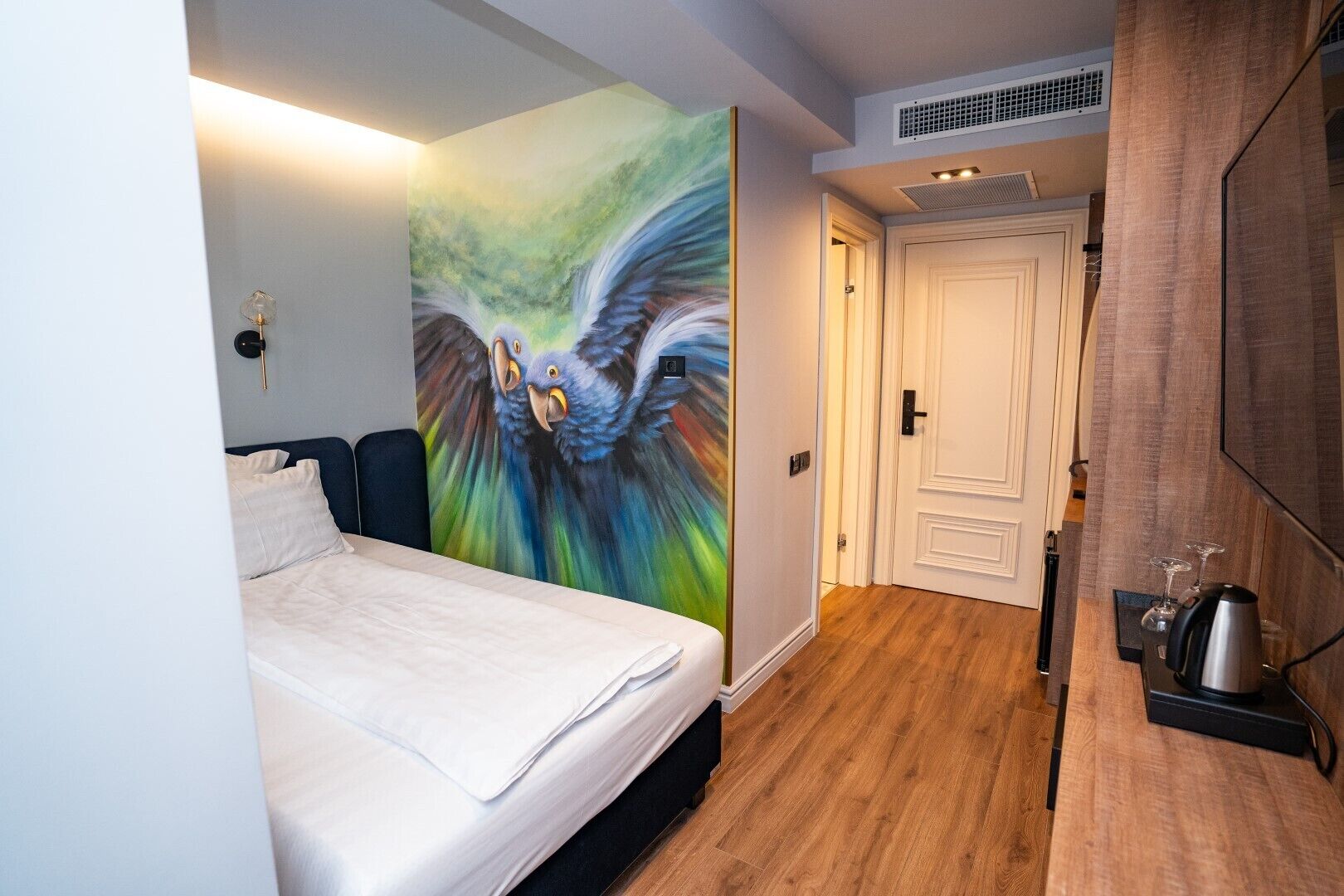 Quarto de hotel com cama, um mural na parede, uma porta e um espaço com cozinha.
