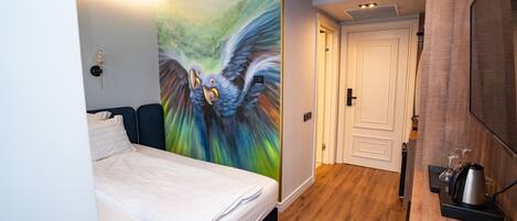 Quarto de hotel com cama, um mural na parede, uma porta e um espaço com cozinha.
