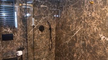 Ein modernes Badezimmer mit einer Glaskabine zur Dusche, einem Holzbadezimmermöbel und Marmorwänden.