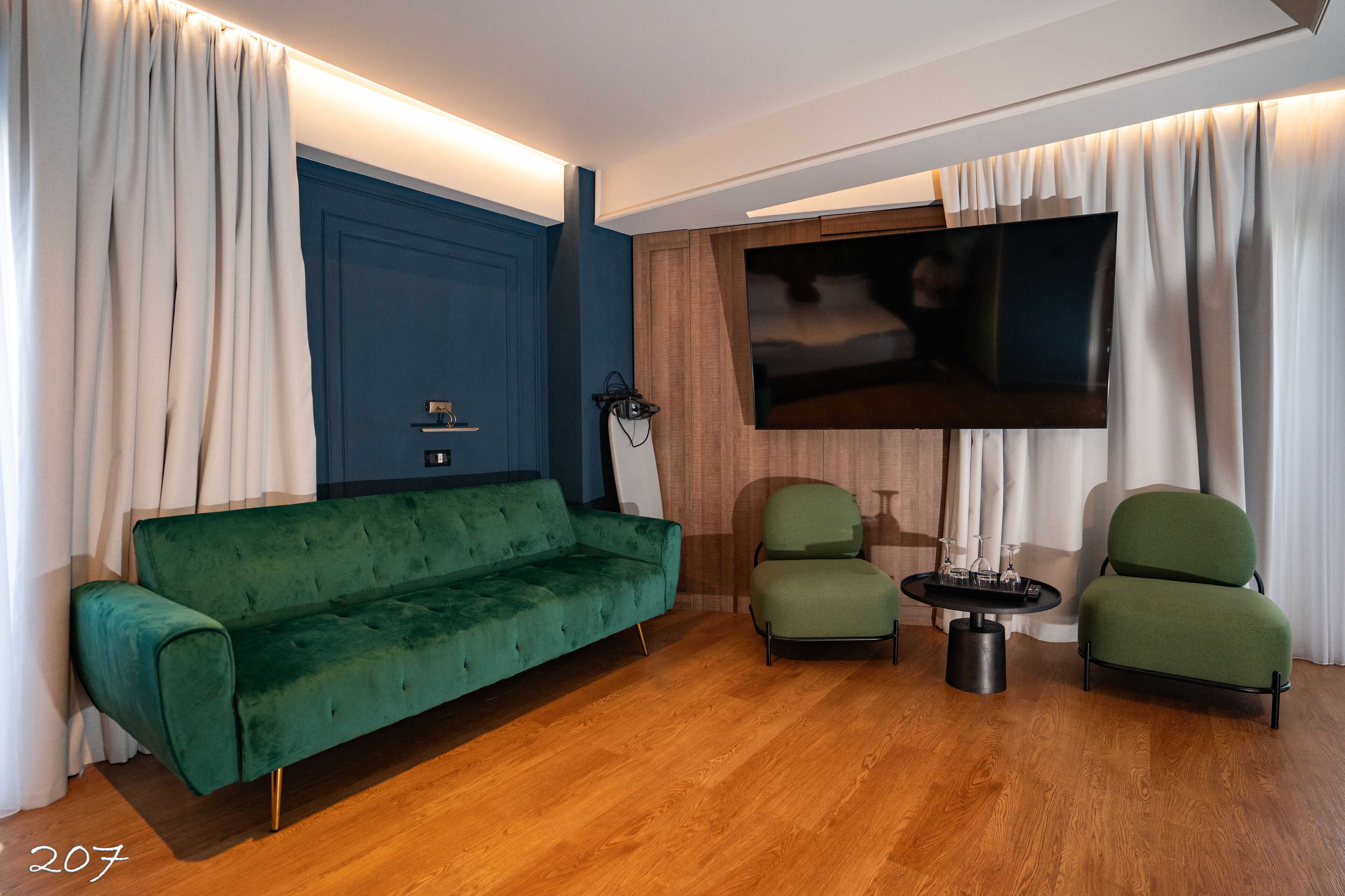 Una sala de estar moderna con un sofá verde, dos sillones, una mesita redonda y un televisor de pantalla plana montado en la pared.