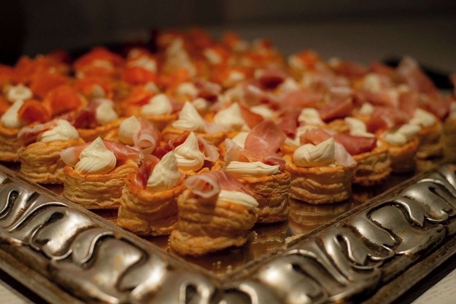 A tray of appetizers with puff pastry cups, topped with cream and slices of ham.