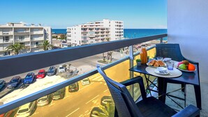 Un balcón con una mesa lista para el desayuno, con vista a una calle y edificios, y una vista del mar.