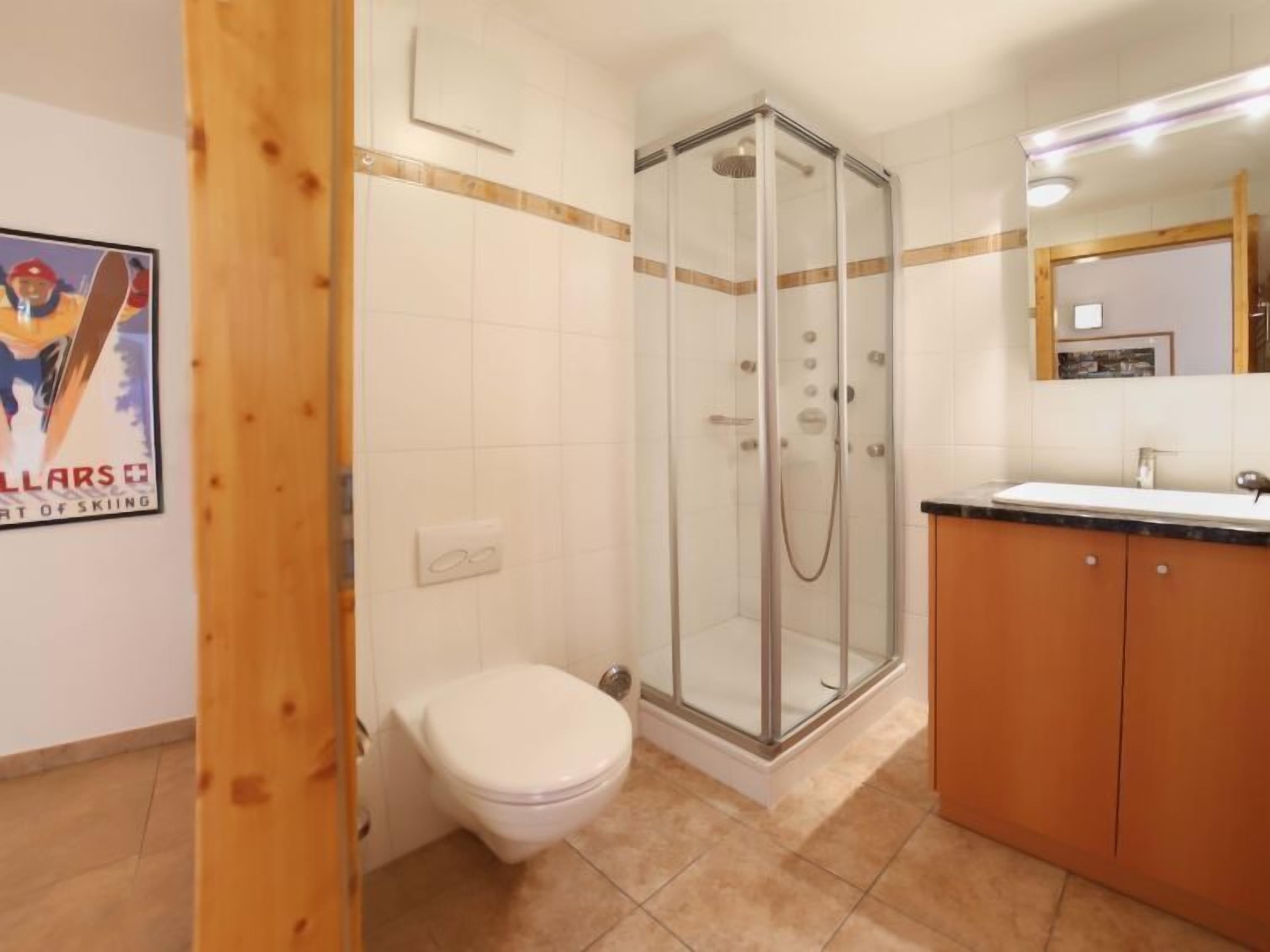 Un baño con inodoro, ducha con mampara de vidrio y un armario de madera.