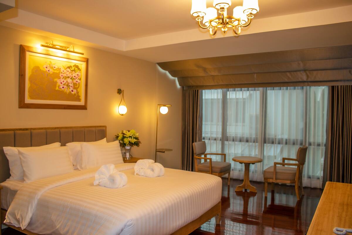 Een hotelkamer met een groot bed, een tafeltje, twee stoelen, een kroonluchter en een schilderij aan de muur.