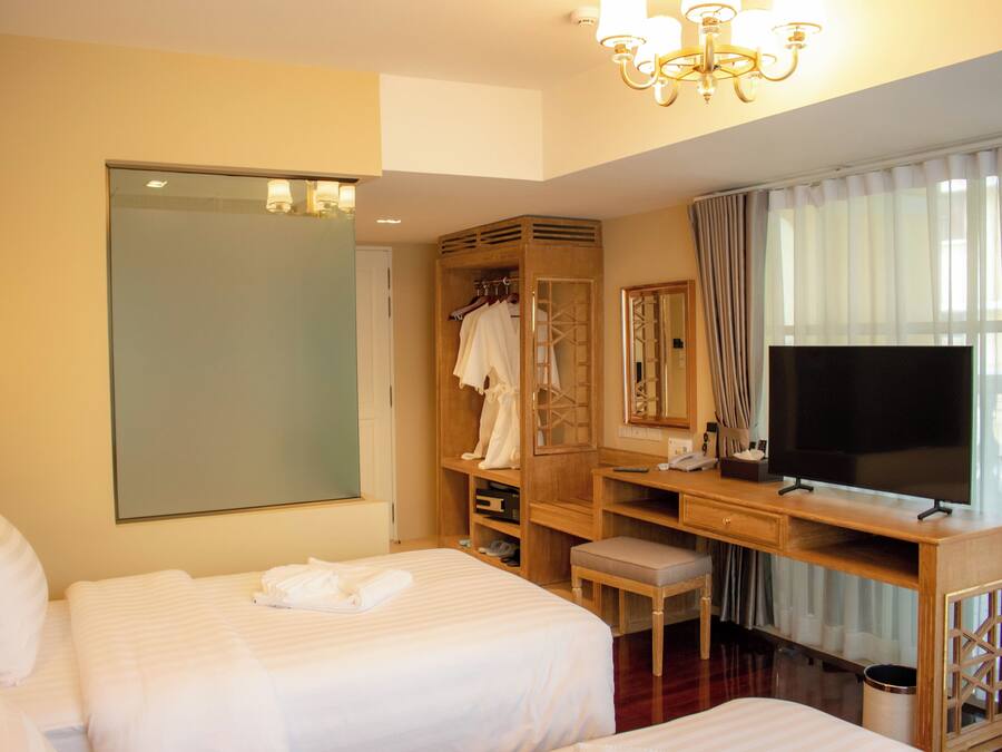 Una habitación de hotel con una cama grande, un escritorio con televisor, un armario y un espejo.