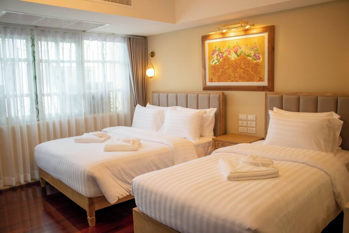 Een hotelkamer met twee bedden, witte lakens, een schilderij aan de muur en een raam met gordijnen.