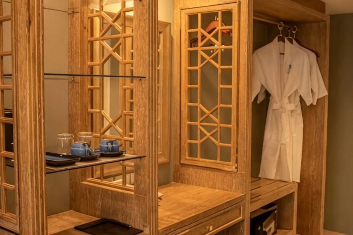 Een houten inloopkast met een badjas aan een rek, een plank met toiletartikelen en een spiegel.
