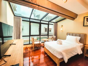 Une chambre d’hôtel comprenant un lit, un bureau, une chaise, une petite table et une grande fenêtre donnant sur des immeubles.