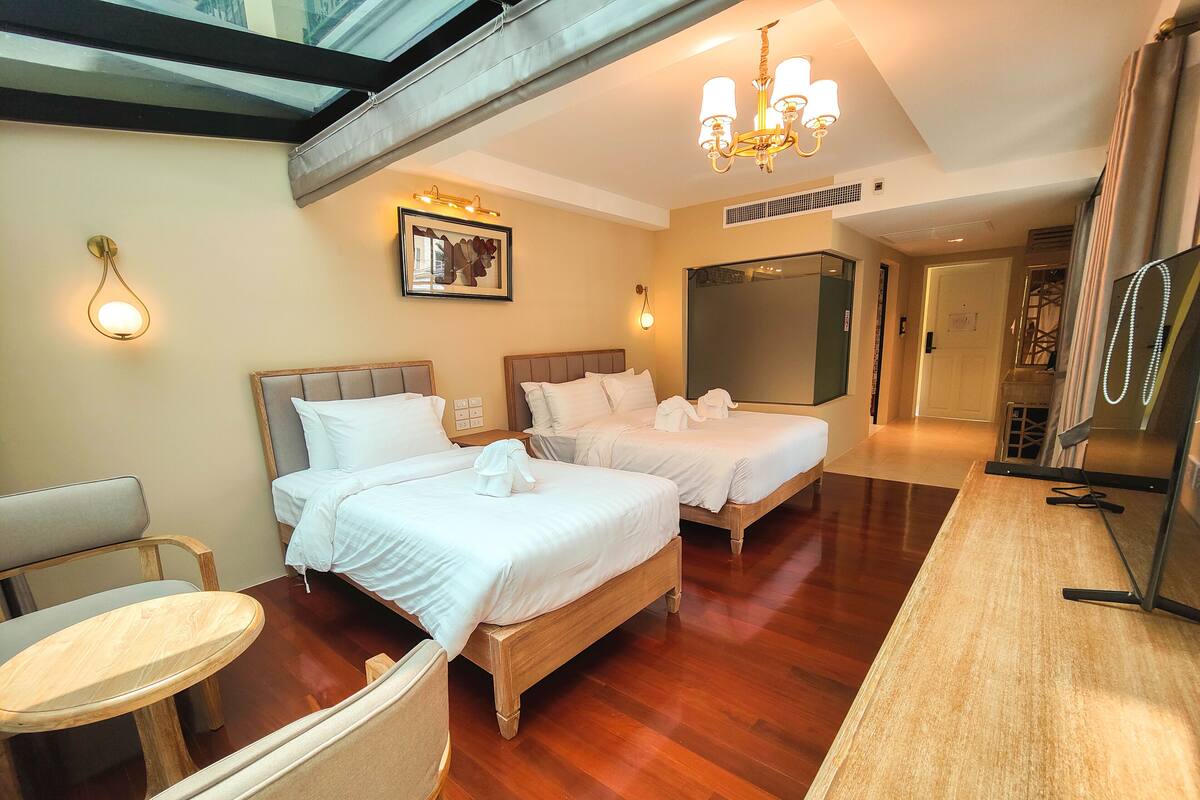 Een hotelkamer met twee bedden, een houten vloer, een kroonluchter, een ingelijste foto aan de muur en een spiegel aan de rechterkant.