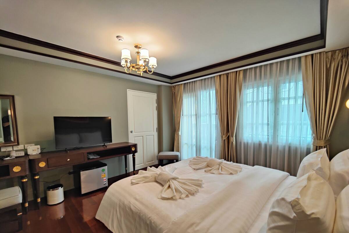 Een hotelkamer met een groot bed, een televisie op een houten bureau, een witte deur en een raam met gordijnen.