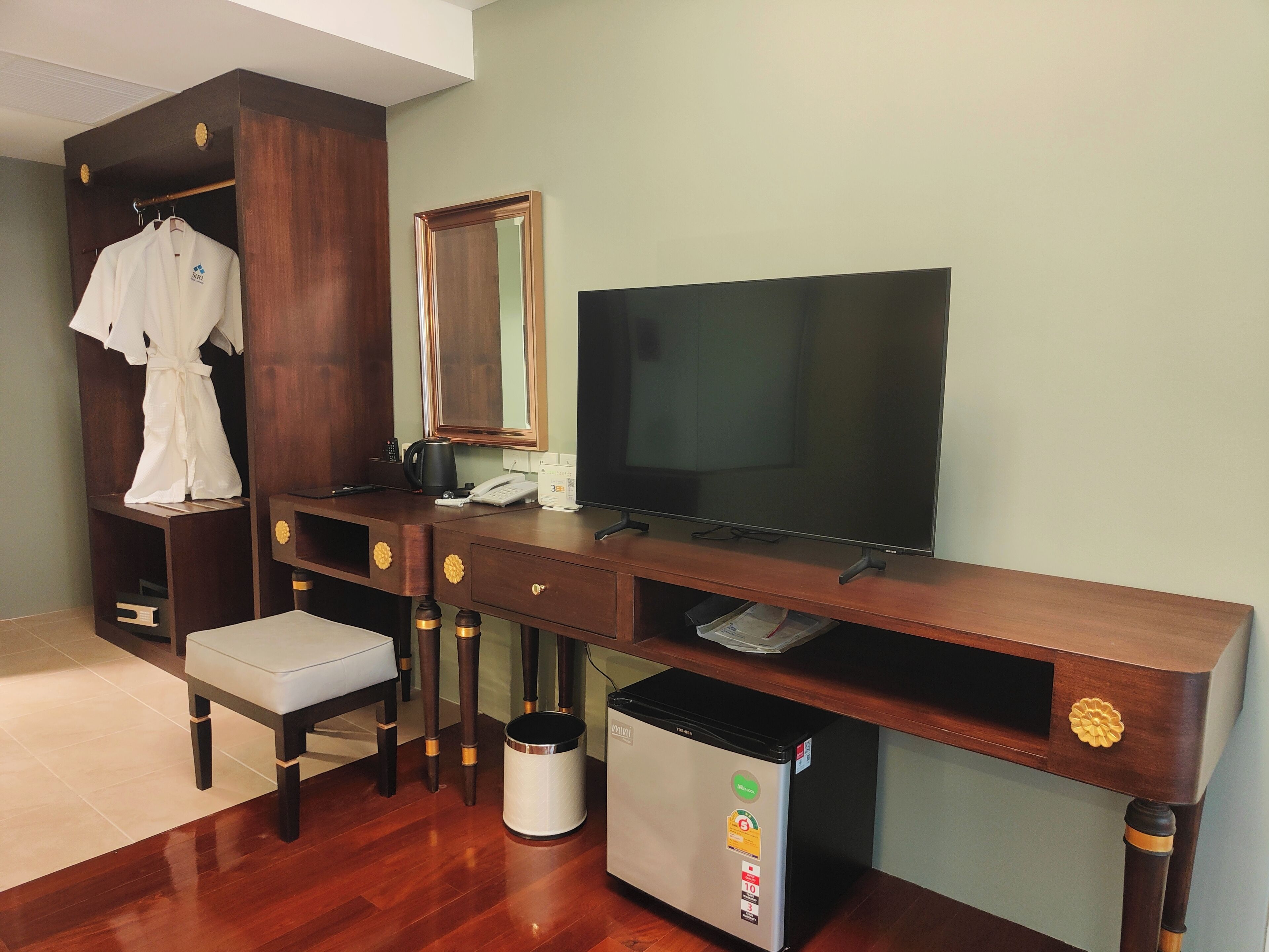 Quarto de hotel com escrivaninha de madeira, televisão, roupão e cesto de lixo.