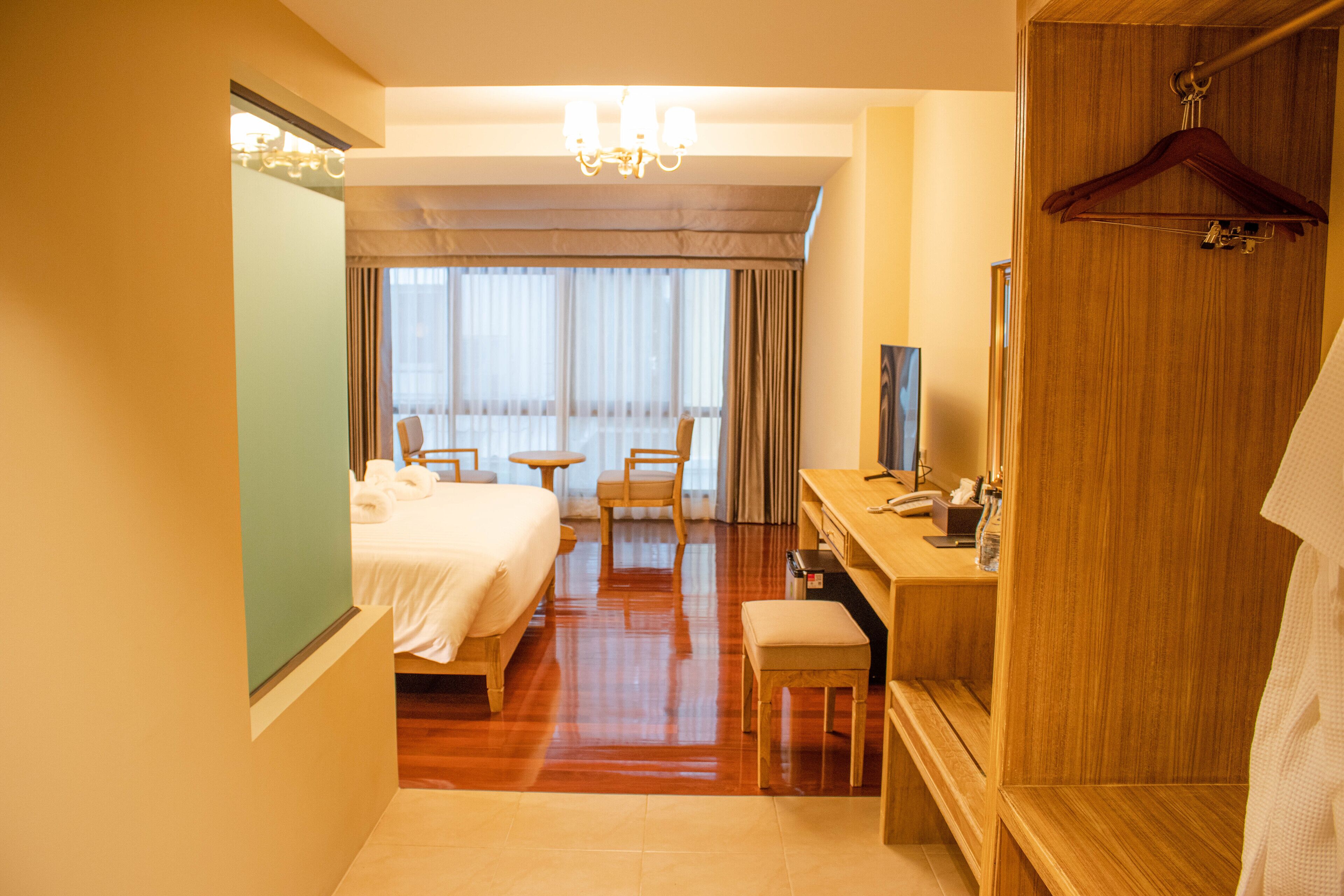 A hotel room with a bed, desk, chair, and a large window with curtains.