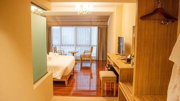 A hotel room with a bed, desk, chair, and a large window with curtains.