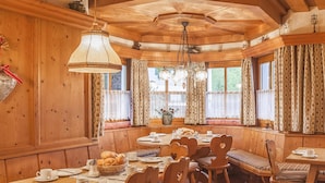 Uma sala de jantar de madeira com teto alto, grandes janelas com cortinas e um lustre.
