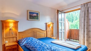 Quarto com cama de madeira, duas mesas de cabeceira com luminárias, uma janela com cortinas e um quadro na parede.