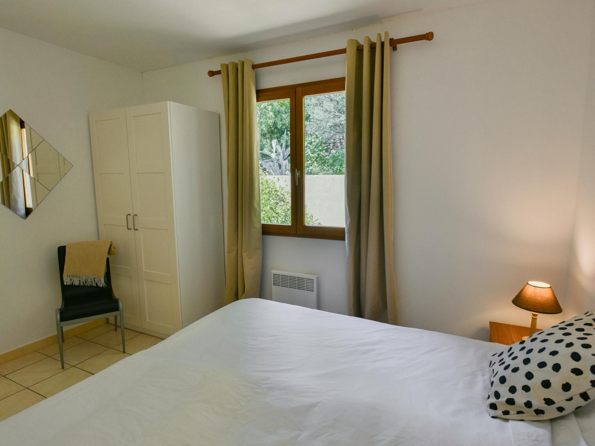 Une chambre à coucher comprenant un lit, une chaise, une armoire, une fenêtre avec des rideaux et une lampe de chevet.