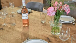 Ett matbord i trä med en vinflaska, tomma glas och en vas med blommor.