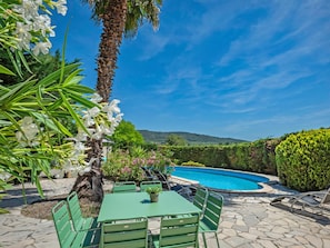 A poolside area with a table and chairs, surrounded by greenery and a clear blue sky. - Villa with private pool and vineyard views (Beaufort)