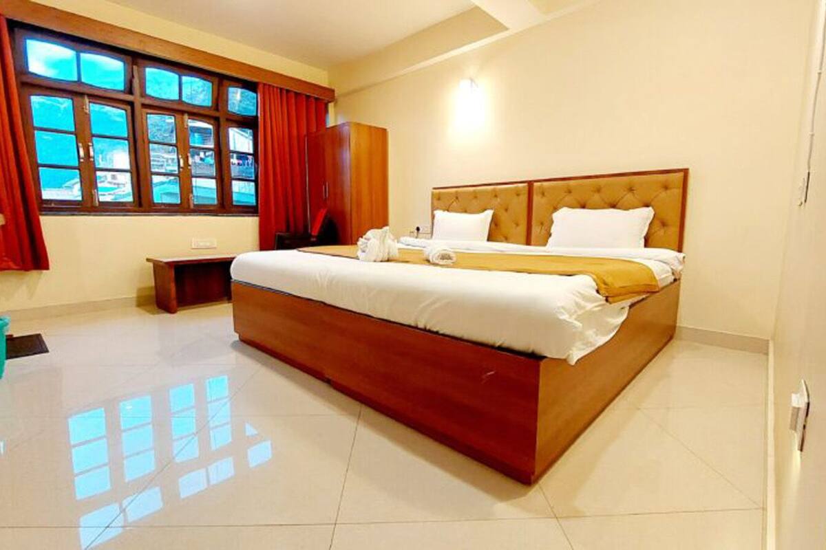 Una cama grande con cabecera de madera, una mesita de noche y una ventana con cortinas.