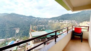 A balcony with a view of a mountainous town, a red chair, and a railing. - Parasol Inn Sikkim  (Gangtok)