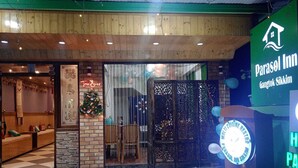 A hotel entrance with a sign for ParaSol Inn Gangtok Sikkim, a multi-cuisine restaurant, and a reception area with a Christmas tree. - Parasol Inn Sikkim  (Gangtok)