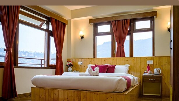 A wooden-framed bed with white and red bedding, a red rug, and a nightstand with a kettle. - Parasol Inn Sikkim  (Gangtok)