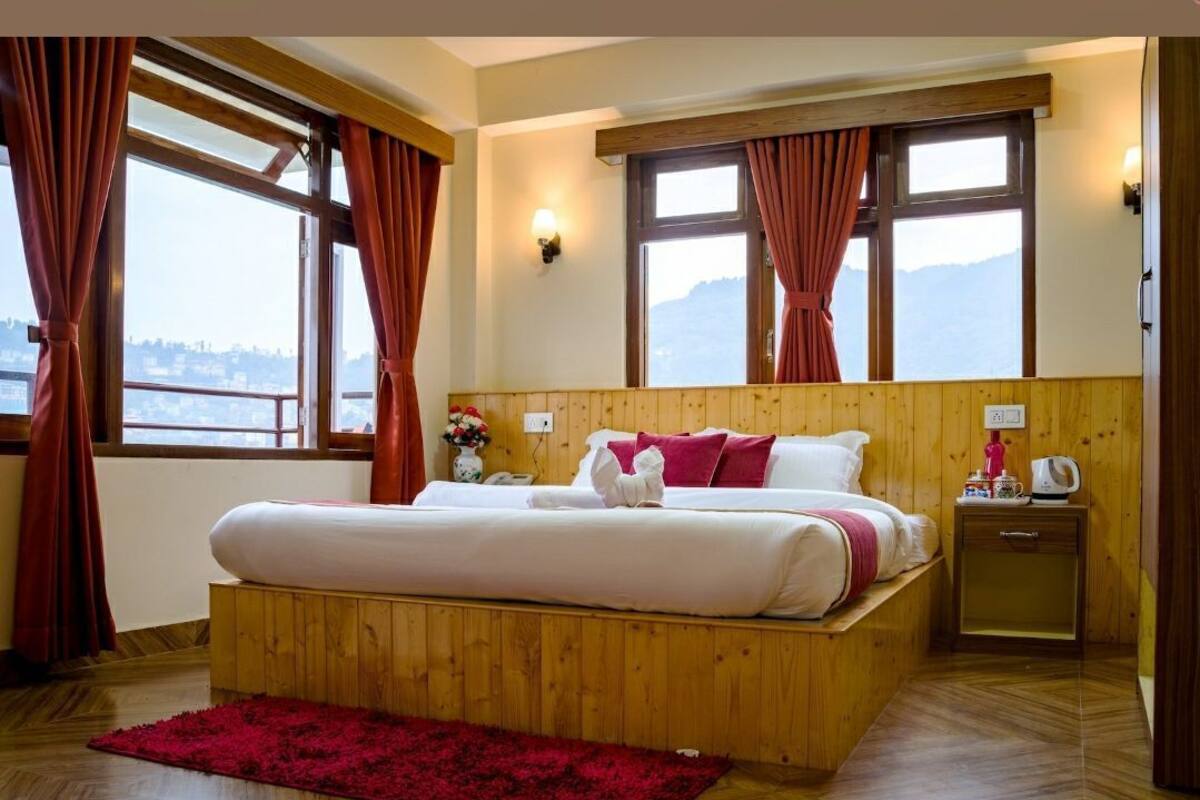 Una cama con estructura de madera, ropa de cama blanca y roja, una alfombra roja y una mesita de noche con un hervidor.