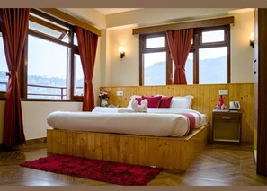 A wooden-framed bed with white and red bedding, a red rug, and a nightstand with a kettle. - Parasol Inn Sikkim (Gangtok)