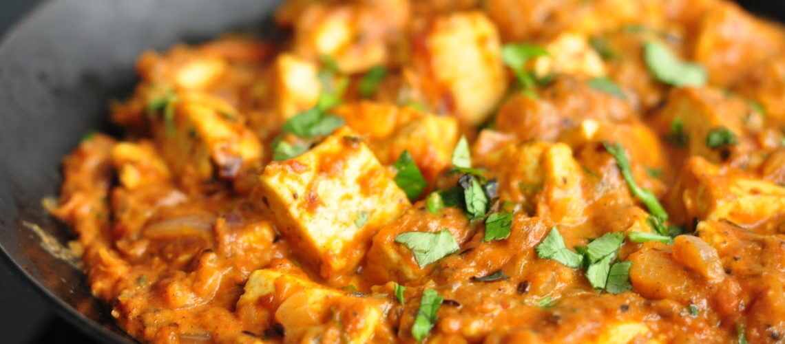 A close-up of paneer curry with chunks of paneer and a garnish of fresh herbs.