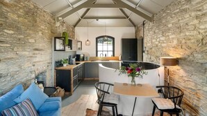 A kitchen with a stone wall, a dining area with a table and chairs, and a blue sofa. - Castle by the Beach with Sea Views, Portreath (Redruth)