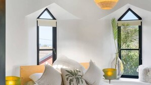 A bedroom with a bed, pillows, a lamp, a vase with a plant, and a window with a view. - Castle by the Beach with Sea Views, Portreath (Redruth)