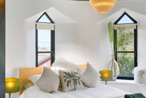 A bedroom with a bed, pillows, a lamp, a vase with a plant, and a window with a view. - Castle by the Beach with Sea Views, Portreath (Redruth)