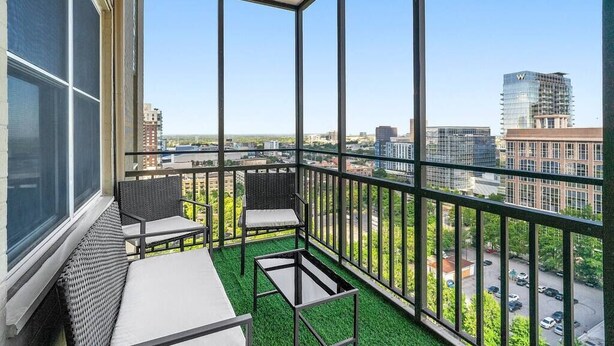 En balkon med udsigt over bybilledet, møbleret med et bord og stole, samt et grønt kunstgræs gulv.