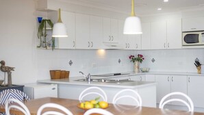 A modern kitchen with white cabinets, a central island with a sink, and pendant lighting. - Bimbajong Main Beach - Pet Friendly- Oceanstays (Yamba)