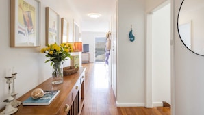 A hallway with framed pictures, a wooden table with flowers, a vase, and a book. - Bimbajong Main Beach - Pet Friendly- Oceanstays (Yamba)
