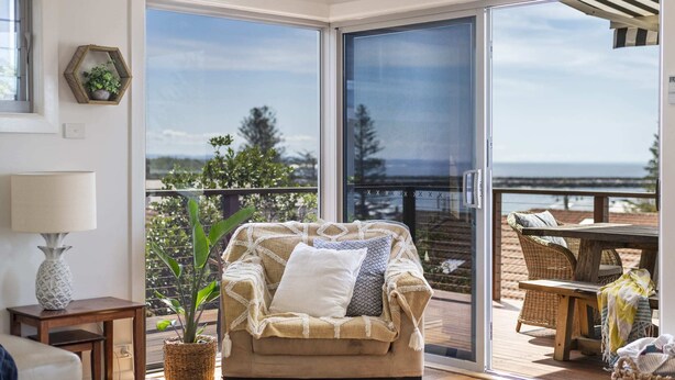 A cozy living room with a large sliding glass door leading to a balcony with a view of the ocean. - Bimbajong Main Beach - Pet Friendly- Oceanstays (Yamba)