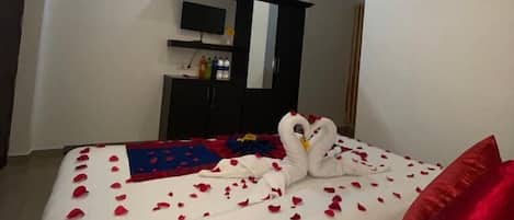 Een moderne hotelkamer met een bed versierd met rozenblaadjes en een zwaan, een plafondventilator en een aan de muur bevestigde televisie.
