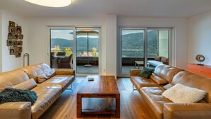 A modern living room with leather sofas, a wooden coffee table, and a large window offering a view of mountains. - Grosse Freiheit alpe maritima Ski&See-17 by Interhome (Ossiacher See)