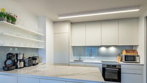 A modern kitchen with white cabinetry, a marble countertop, and built-in appliances including a coffee maker, toaster, and microwave. - Grosse Freiheit alpe maritima Ski&See-17 by Interhome (Ossiacher See)