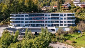 A multi-story hotel with a modern design, featuring balconies on each floor and a parking area in front. - Grosse Freiheit alpe maritima Ski&See-17 by Interhome (Ossiacher See)