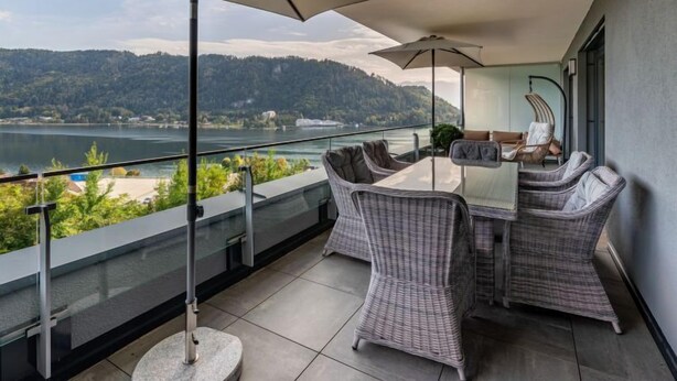A balcony with a table and chairs, a view of a lake, and a mountainous landscape. - Grosse Freiheit alpe maritima Ski&See-17 by Interhome (Ossiacher See)
