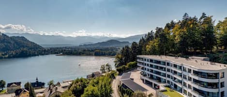 A modern multi-story building with a flat roof, surrounded by lush greenery and a lake.